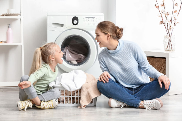 Mutter und Tochter sitzen glücklich vor der Waschmaschine
