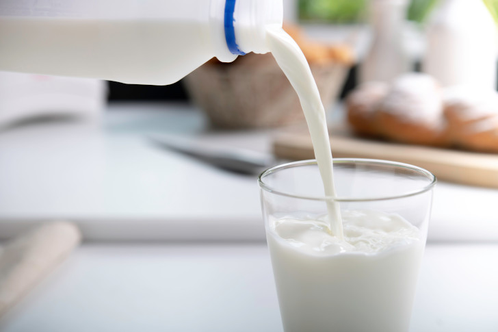 Milch wird in ein Glas gefüllt im Hintergrund sind Backwaren zu sehen