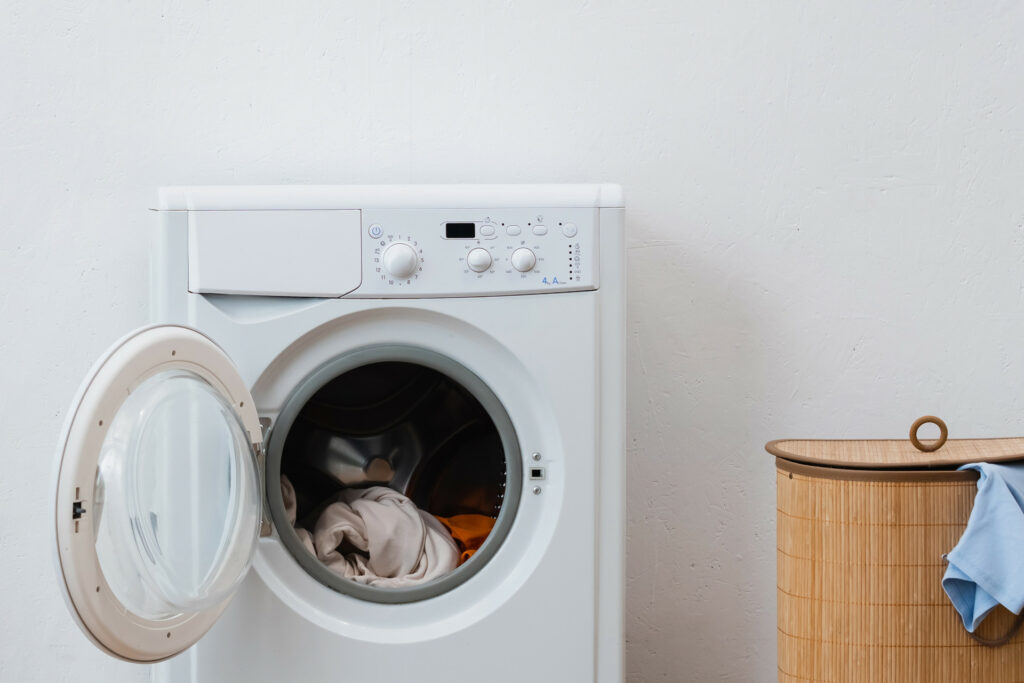 eine weiße Waschmaschine daneben steht ein Holzwäschekorb