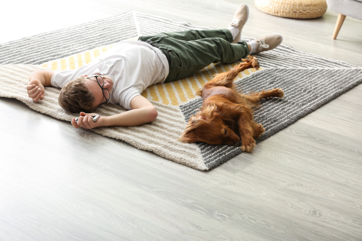 Ein Mann und sein brauner Hund liegen auf einem Teppich auf dem der Geruch entfernt wurde
