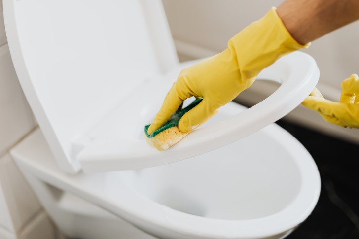 Urinrückstände werden mit einem gelben Schwamm vom Toilettensitz weggeputzt