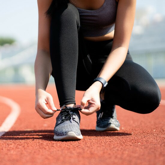 Ein Sportwaschmittel ist sinnvoll für jeden, der gerne geruchsfrei Sport treiben will eine Frau bindet sich ihre grauen Laufschuhe auf einer roten Tartanbahn