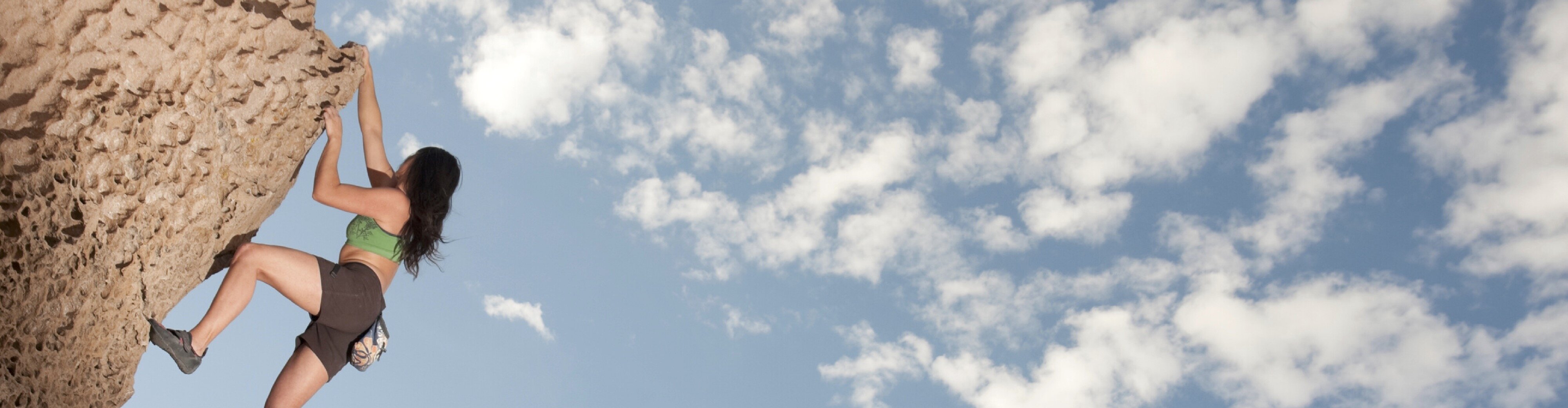 eine Frau klettert eine Felswand bei leicht bewölktem Himmel hinauf