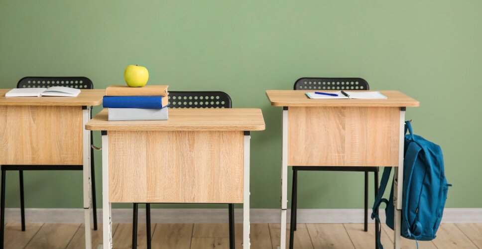 Klassenzimmer mit Schultischen und einem blauen Rucksack